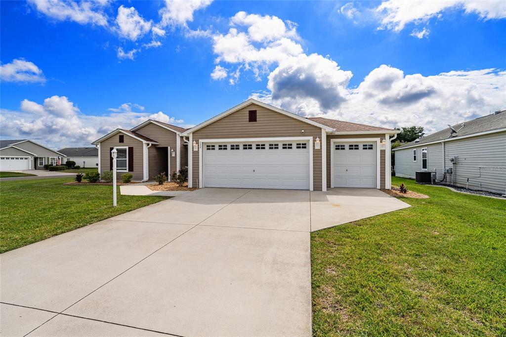 A tan, single-story suburban house with a three-car garage and a concrete driveway — 2446 HOPESPRING LOOP, THE VILLAGES, FL