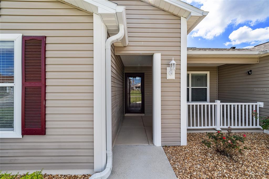 The exterior of a house features beige siding, a recessed entryway, and a white railing — 2446 HOPESPRING LOOP, THE VILLAGES, FL