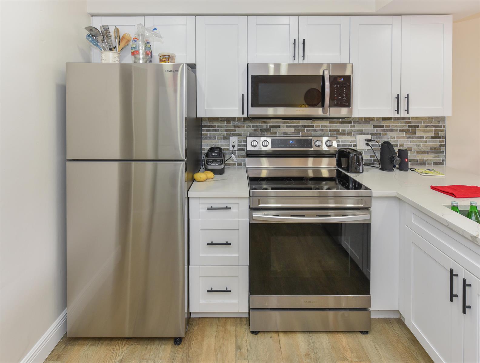 A kitchen features white cabinets, stainless steel appliances, and a tiled backsplash — 1605 Us-1 # D305, Jupiter FL 33477, JUPITER, FL