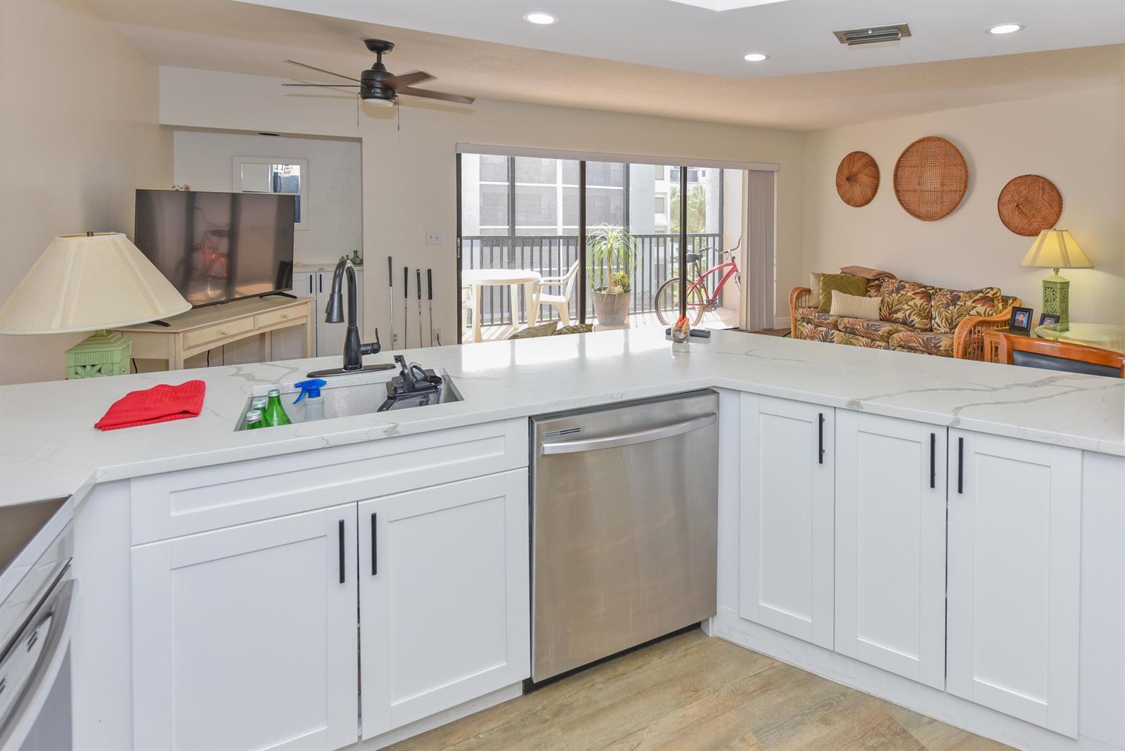 A kitchen with white cabinets, quartz countertops, and a stainless steel dishwasher overlooks a living area — 1605 Us-1 # D305, Jupiter FL 33477, JUPITER, FL