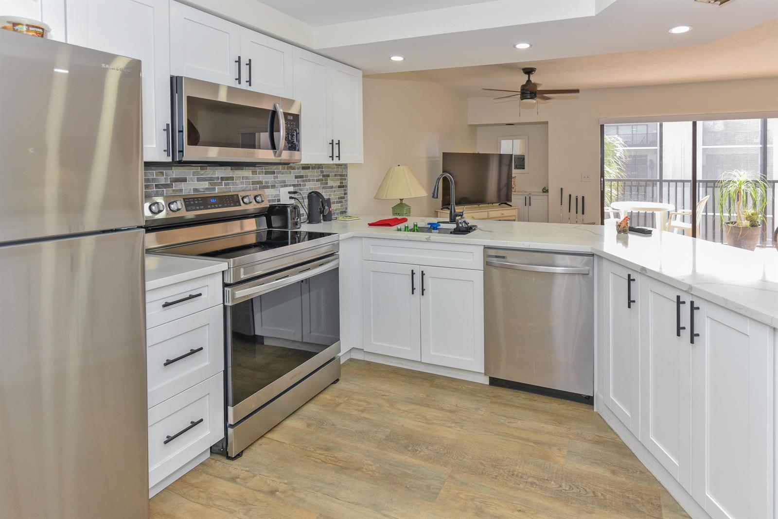A kitchen features white cabinets, stainless steel appliances, and a peninsula overlooking a living area — 1605 Us-1 # D305, Jupiter FL 33477, JUPITER, FL