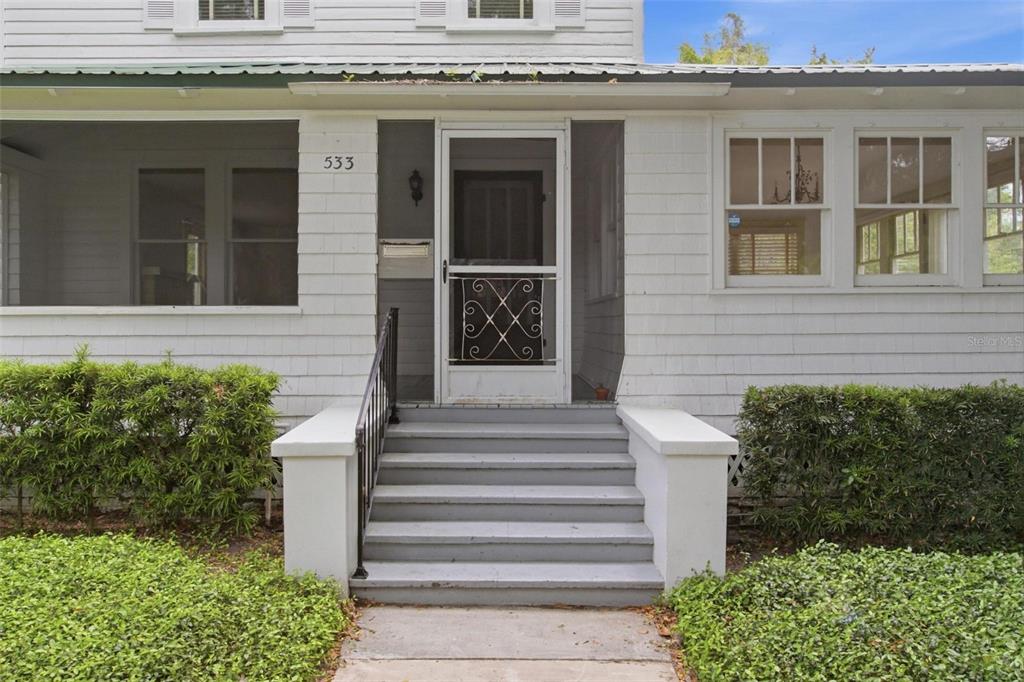 A white house exterior features a front porch, gray steps, and a screen door — 533 N SANS SOUCI AVENUE, DELAND, FL