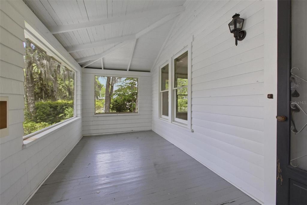 A white-walled covered porch features a gray wooden floor, large windows, and a wall-mounted lantern — 533 N SANS SOUCI AVENUE, DELAND, FL