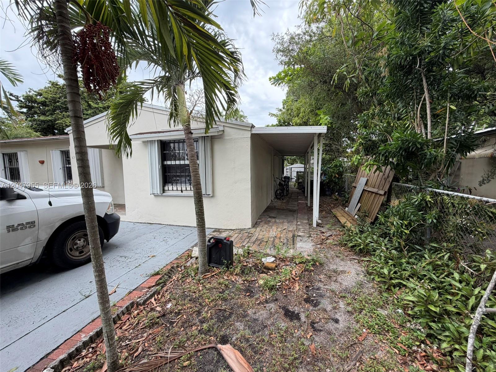 A white house with a carport, a brick walkway, and palm trees in the front yard — 596 NW 109th St, Miami FL 33168, MIAMI, FL