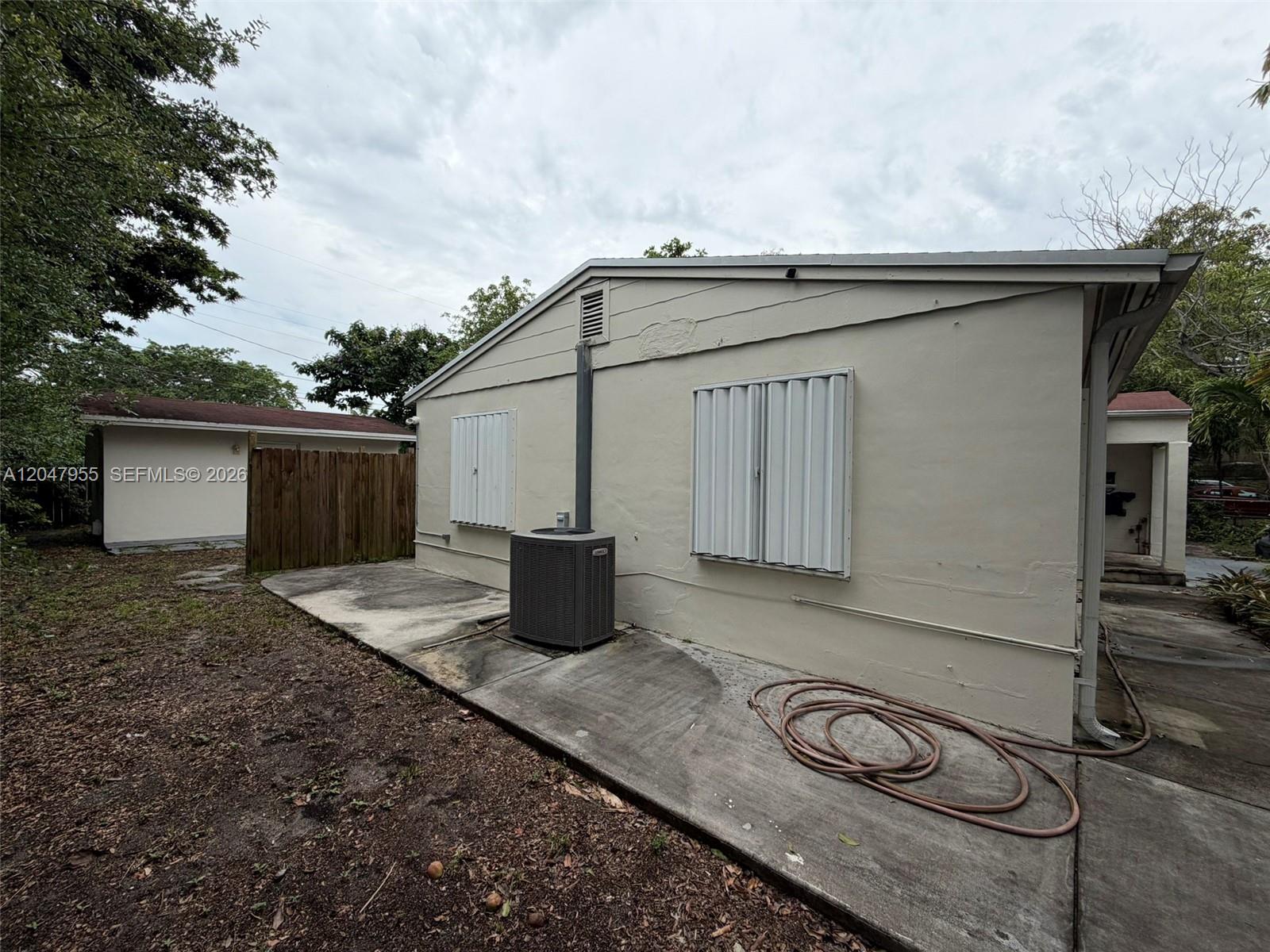 The exterior of a house features a concrete patio, an HVAC unit, and storm shutters — 596 NW 109th St, Miami FL 33168, MIAMI, FL