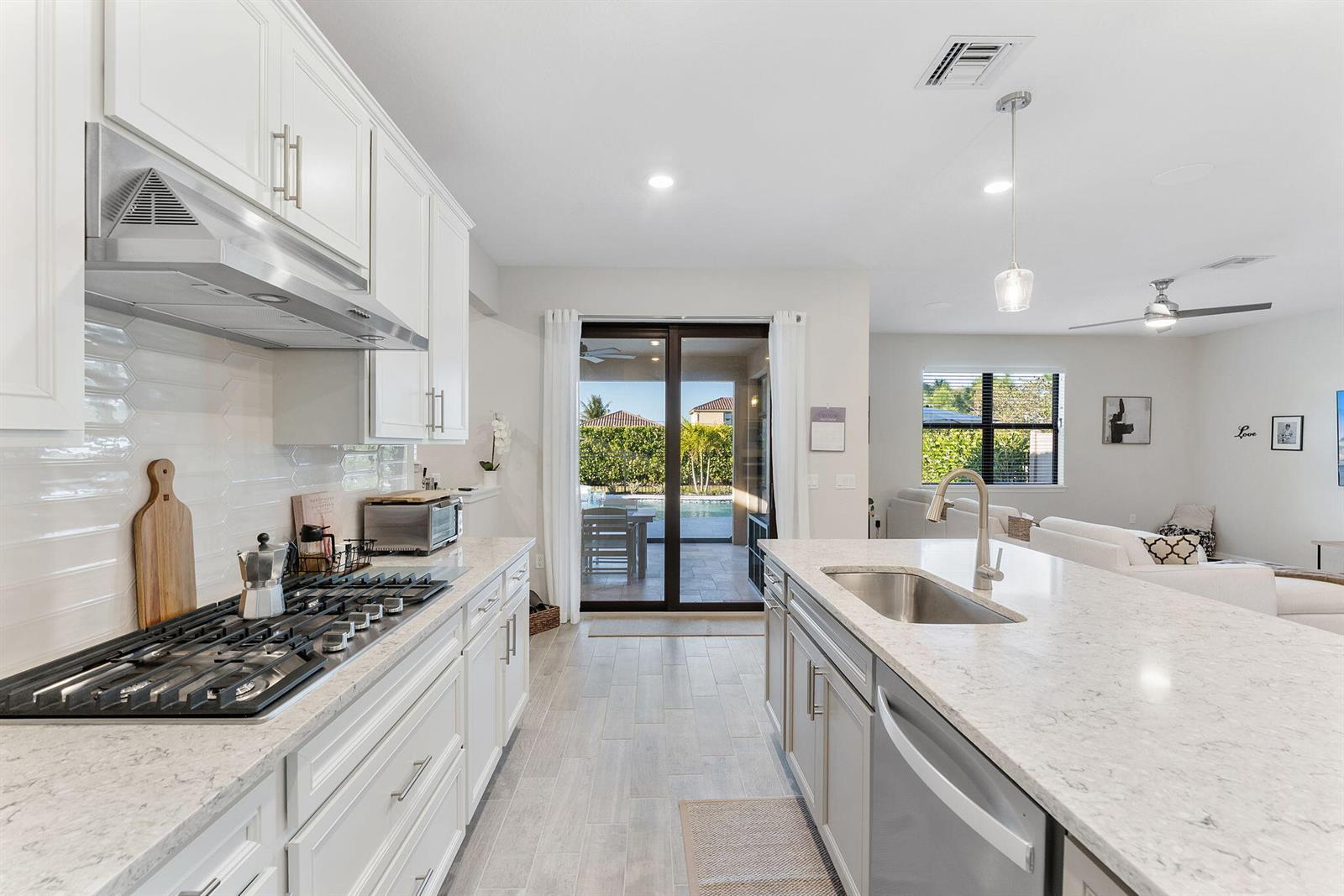 A modern kitchen features white cabinets, a large island with a sink, and sliding glass doors — 8623 Patron Lane, Lake Worth FL 33467, LAKE WORTH, FL