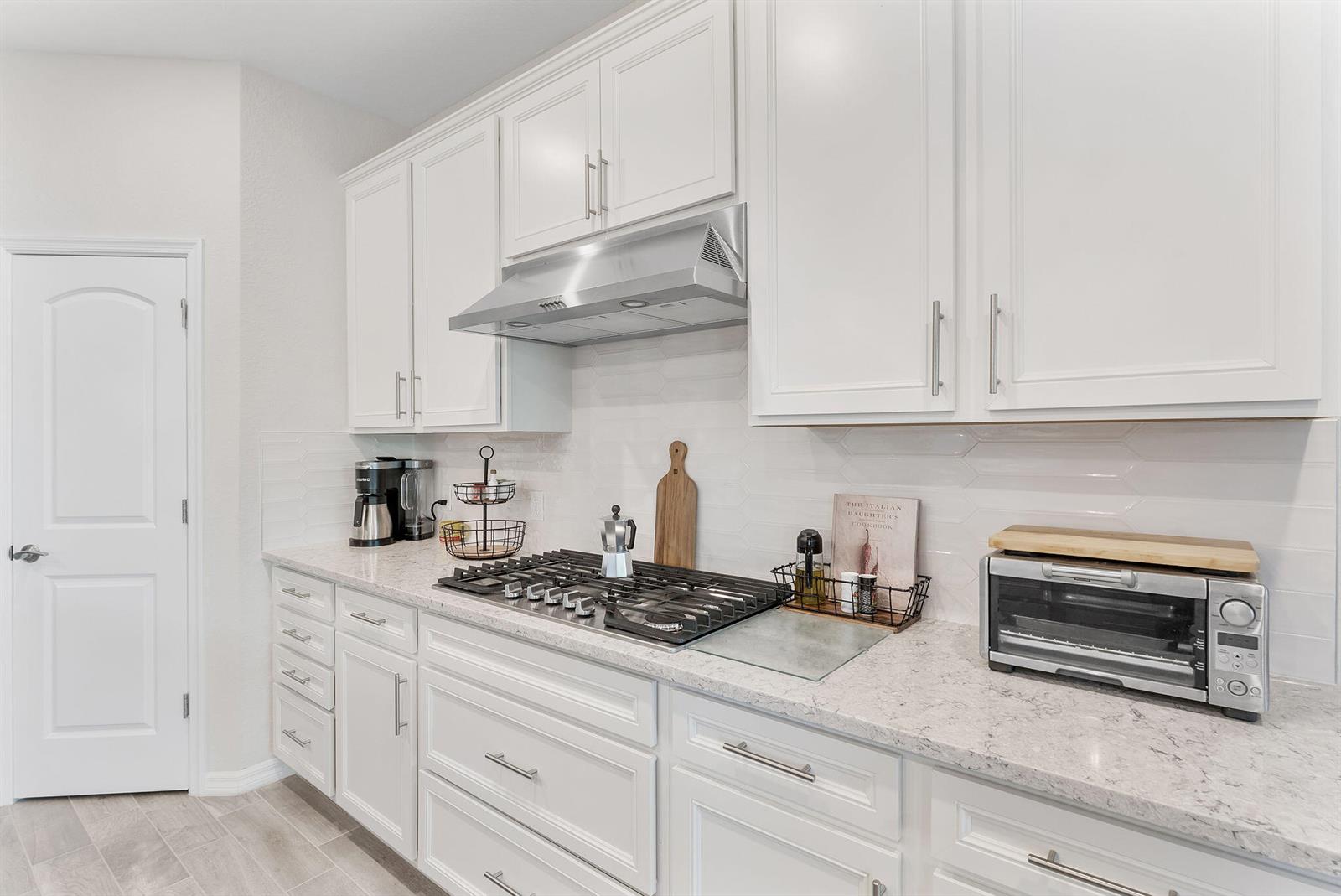 A kitchen features white cabinets, a gas cooktop, a stainless steel hood, and quartz countertops — 8623 Patron Lane, Lake Worth FL 33467, LAKE WORTH, FL