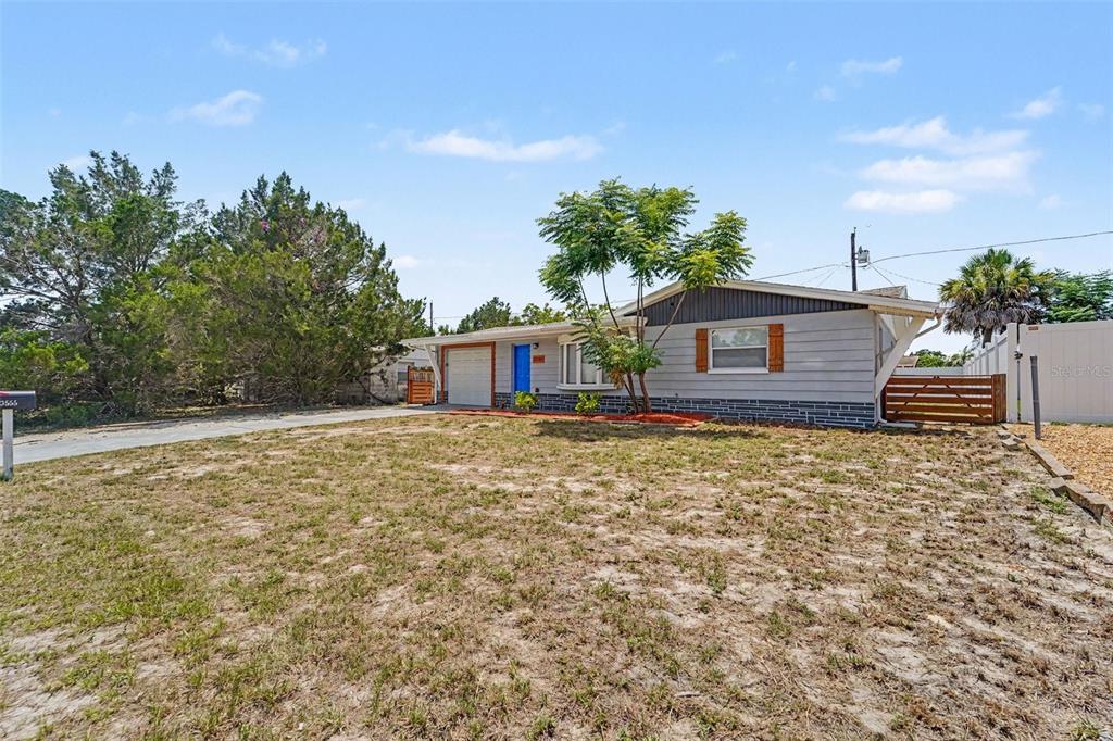 A single-story house with gray siding, a blue front door, and a large front yard — 3555 SHERYL HILL DRIVE, HOLIDAY, FL