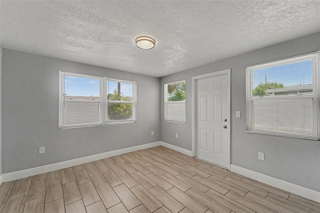 An empty room with gray walls, wood-look tile flooring, a white door, and three windows — 3555 SHERYL HILL DRIVE, HOLIDAY, FL