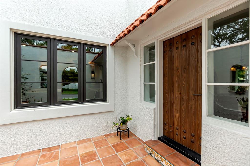 A wooden front door with metal studs sits beside a window on a tiled porch — 1864 CLEMATIS ST STREET, SARASOTA, FL