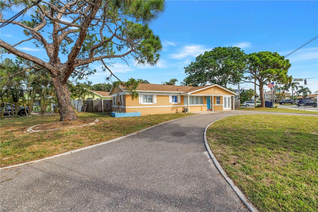 A single-story yellow house with a curved asphalt driveway and a large pine tree — 7901 CAUSEWAY BOULEVARD S, ST PETERSBURG, FL