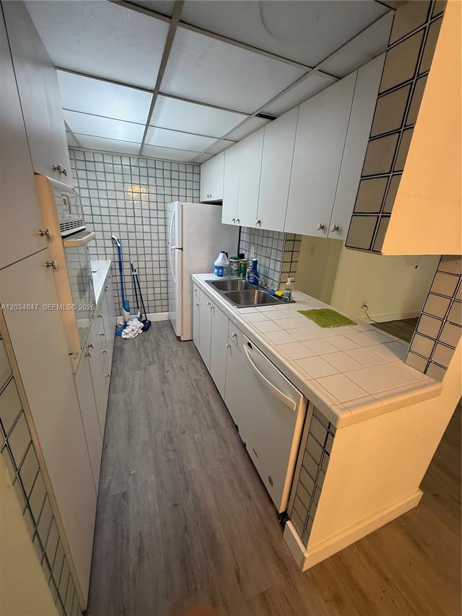 A galley-style kitchen features white cabinets, tiled countertops, a double sink, and a drop ceiling — 2201 Brickell Ave # 67C, Miami FL 33129, MIAMI, FL