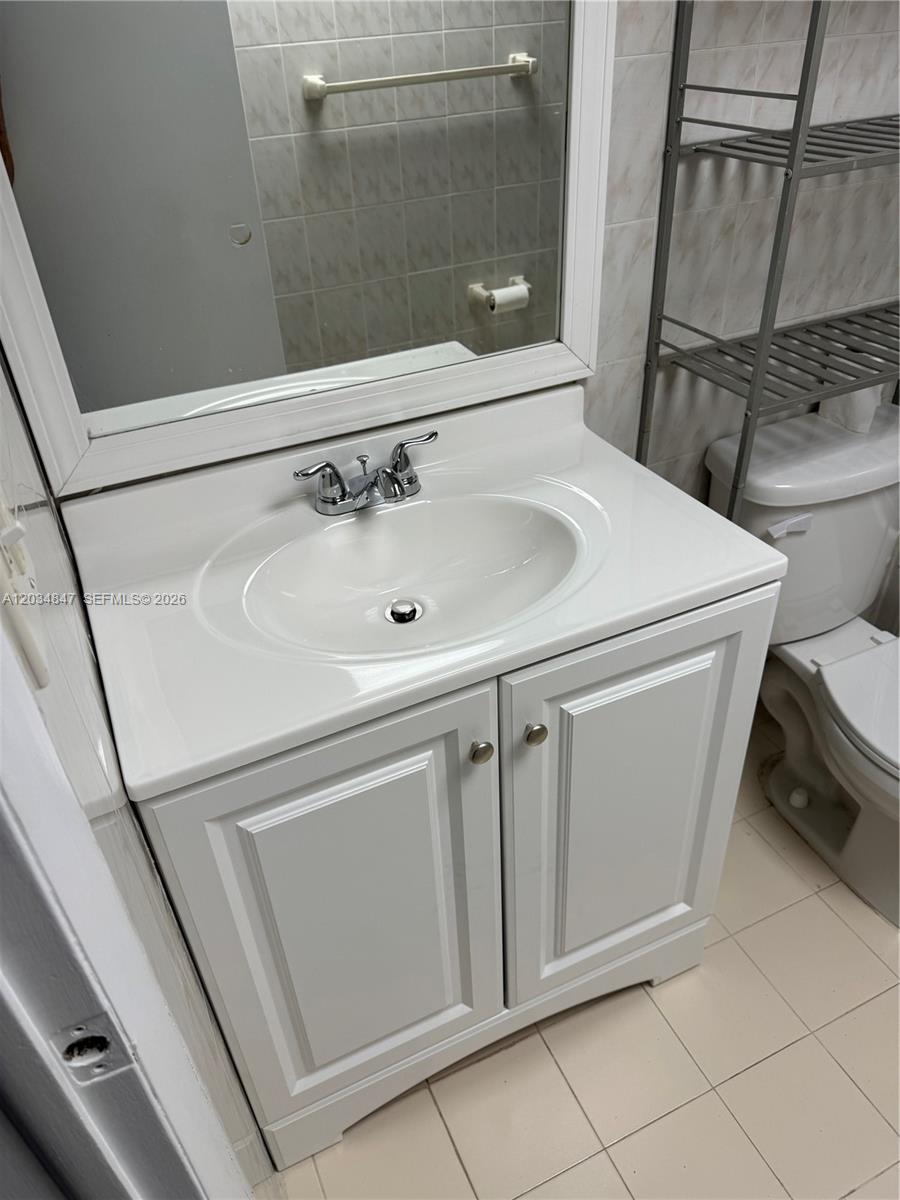 A white bathroom vanity with a chrome faucet sits next to a toilet and shelving — 2201 Brickell Ave # 67C, Miami FL 33129, MIAMI, FL