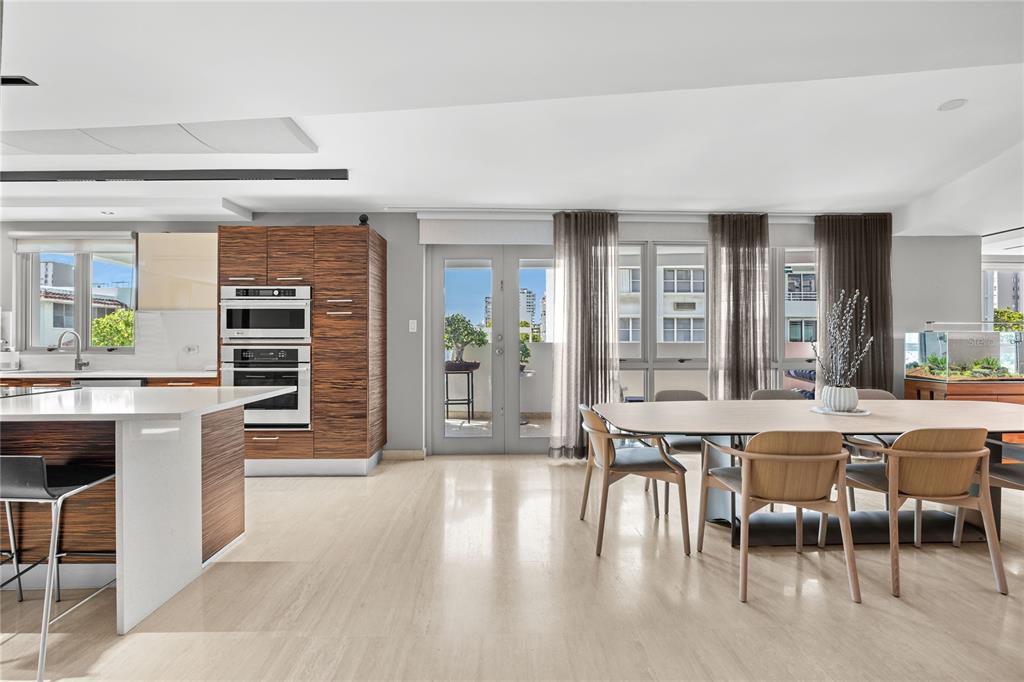 A modern kitchen and dining area featuring wood cabinetry, a white island, and glass doors — 63 MIRSONIA STREET UNIT 401, SAN JUAN, PR