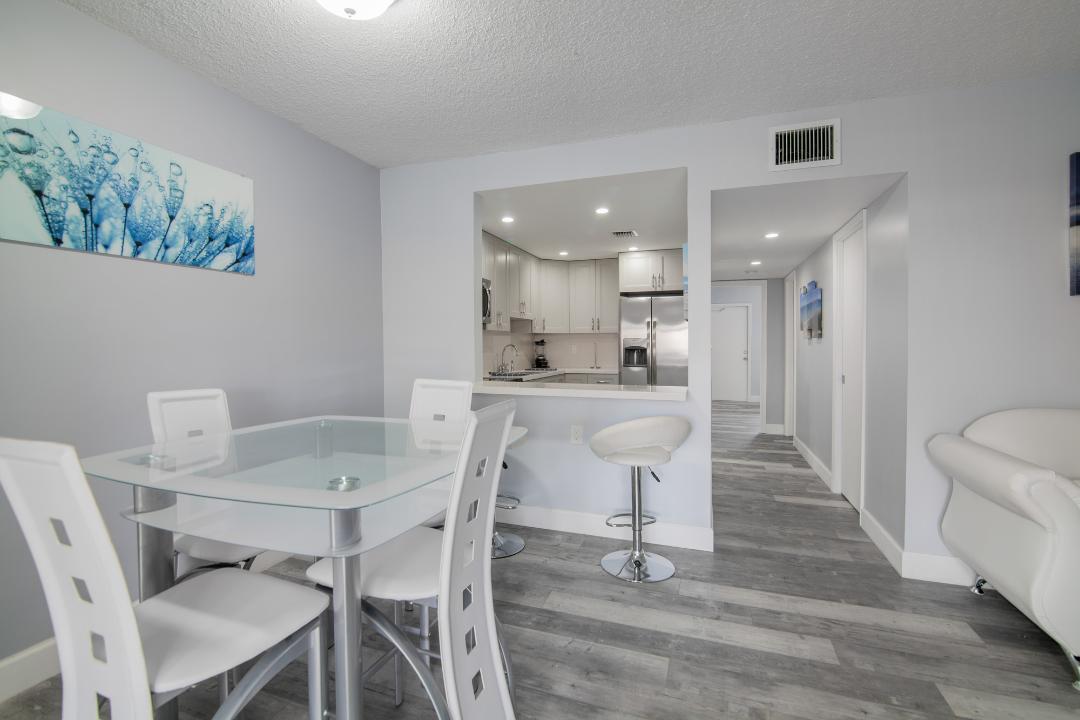 A dining area with a glass table and white chairs opens to a modern kitchen — 320 S Surf Road # 205, Hollywood FL 33019, HOLLYWOOD, FL