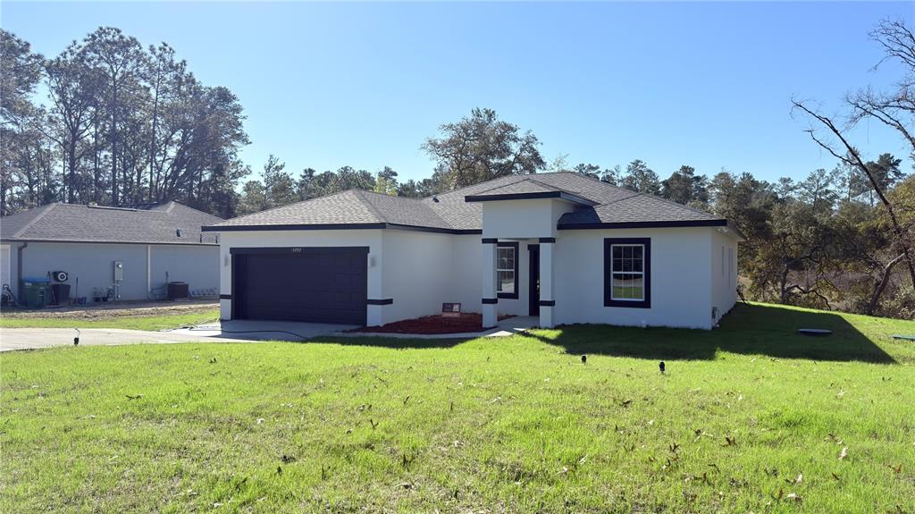 A single-story house with a dark garage door, white stucco exterior, and a concrete driveway — 15777 SW 55TH AVENUE ROAD, OCALA, FL