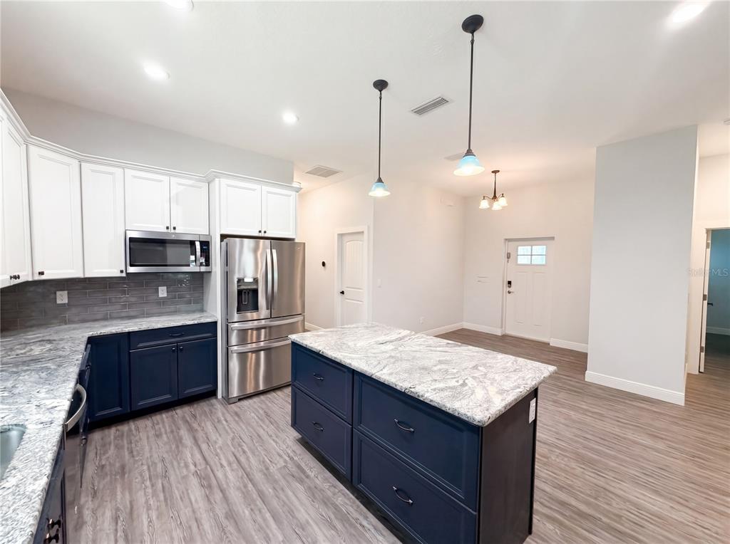 A kitchen features blue lower cabinets, white upper cabinets, granite countertops, and a central island — 2700 WESTSIDE DRIVE, LEESBURG, FL