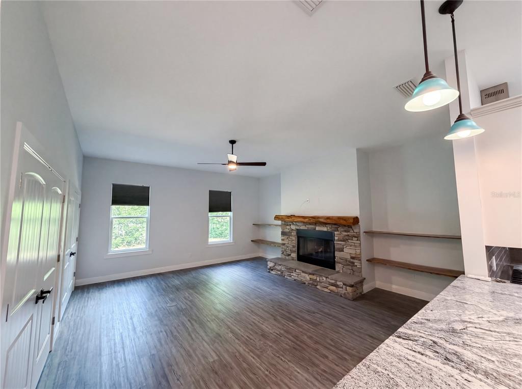 A living room features a stone fireplace, wood shelving, and dark wood-look flooring — 2700 WESTSIDE DRIVE, LEESBURG, FL