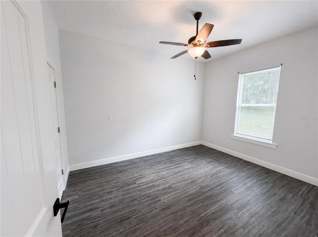 An empty bedroom features gray wood-look flooring, white walls, a ceiling fan, and one window — 2700 WESTSIDE DRIVE, LEESBURG, FL