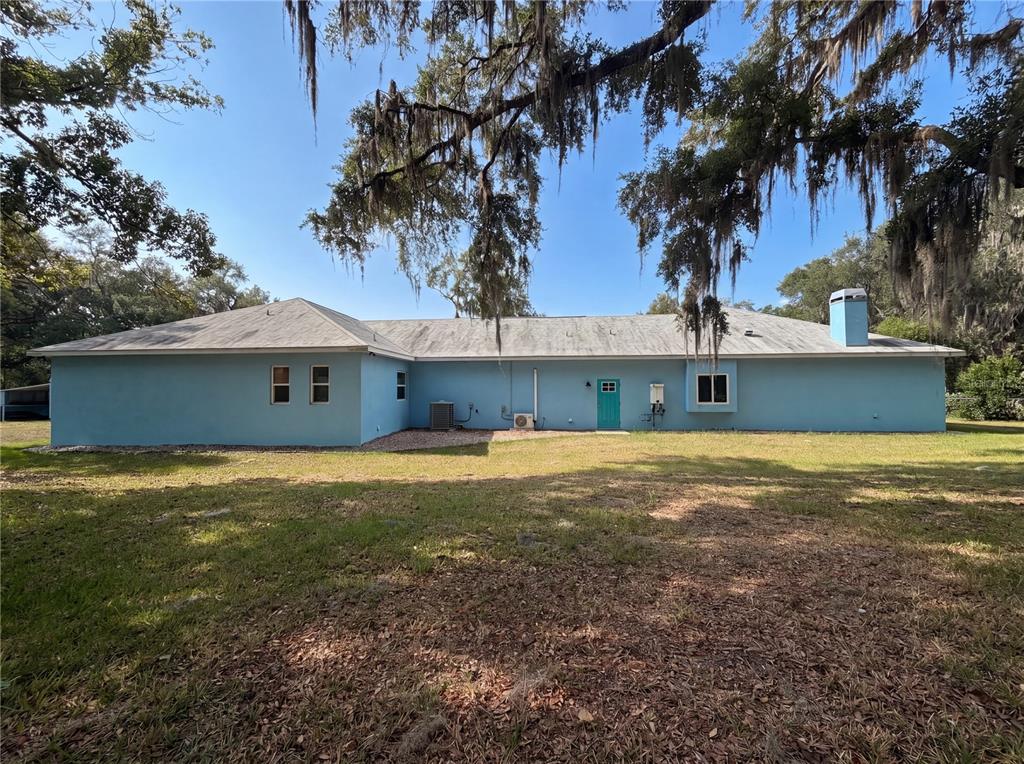 The back exterior of a light blue, single-story house features a teal door and chimney — 2700 WESTSIDE DRIVE, LEESBURG, FL