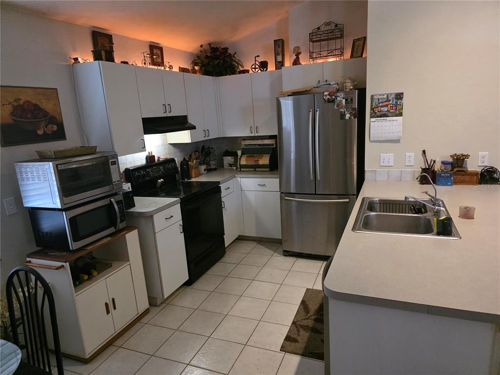 A kitchen features white cabinets, stainless steel appliances, a double sink, and tiled flooring — 1931 SW 73RD STREET, GAINESVILLE, FL