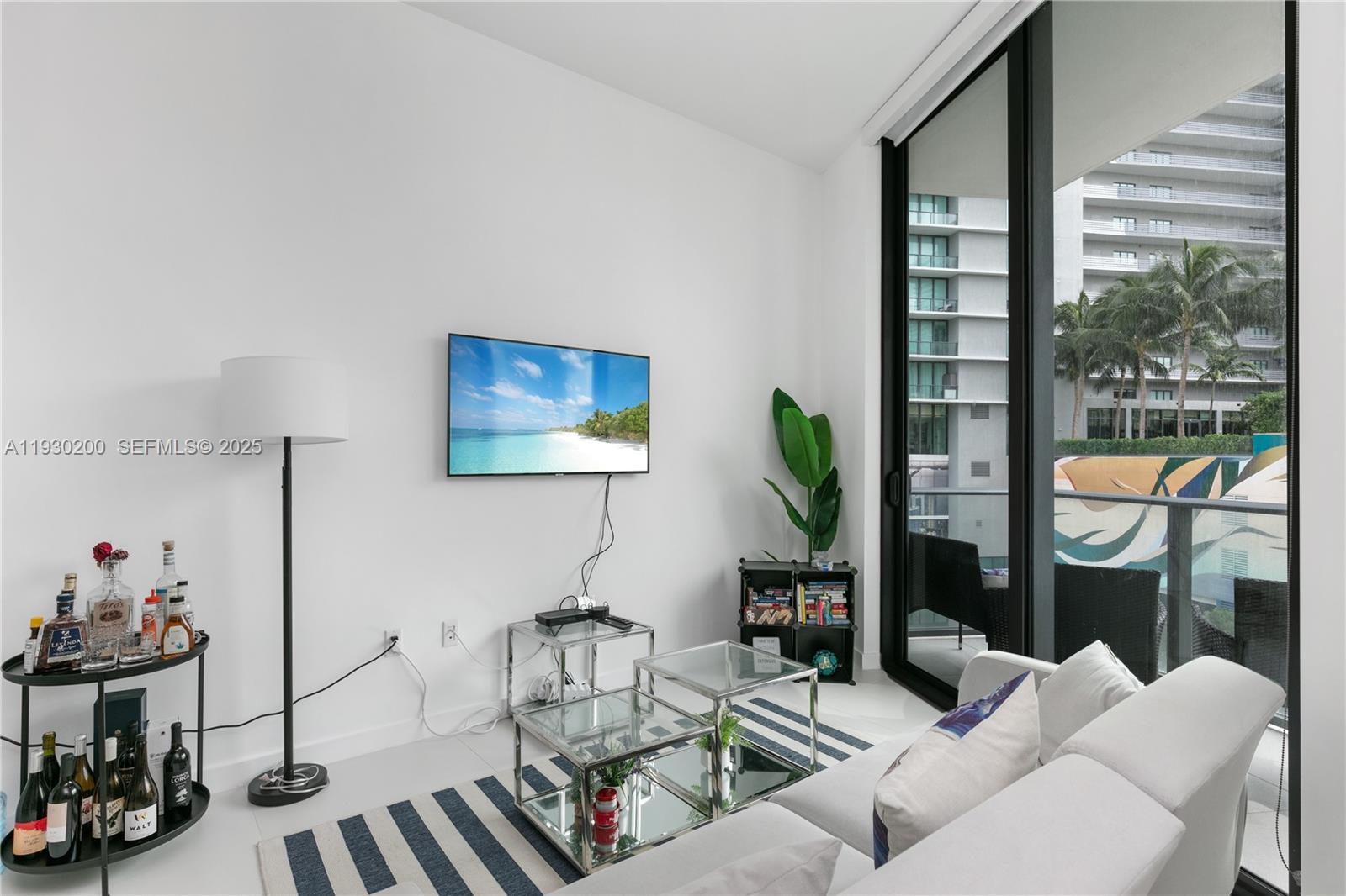 A living room features a wall-mounted television, glass tables, a bar cart, and balcony access — 501 NE 31st St # 307, Miami FL 33137, MIAMI, FL