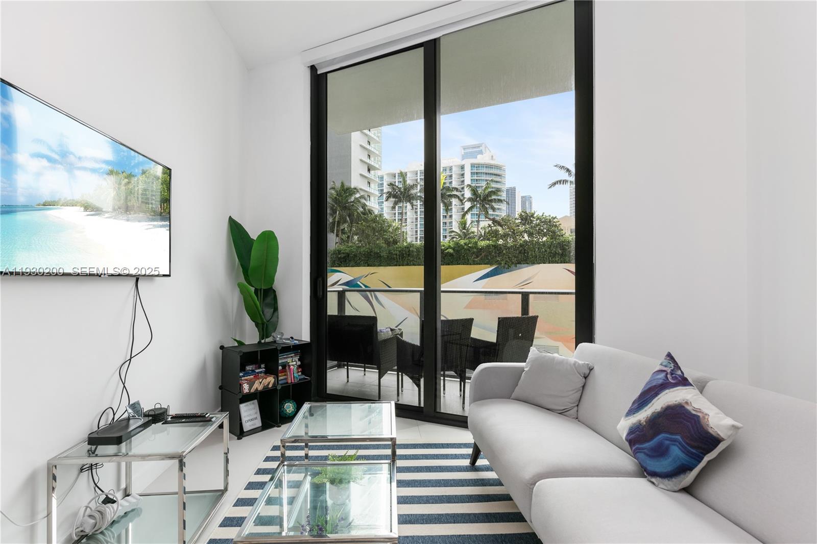 A living room features a grey sofa, glass coffee tables, and a balcony with city views — 501 NE 31st St # 307, Miami FL 33137, MIAMI, FL