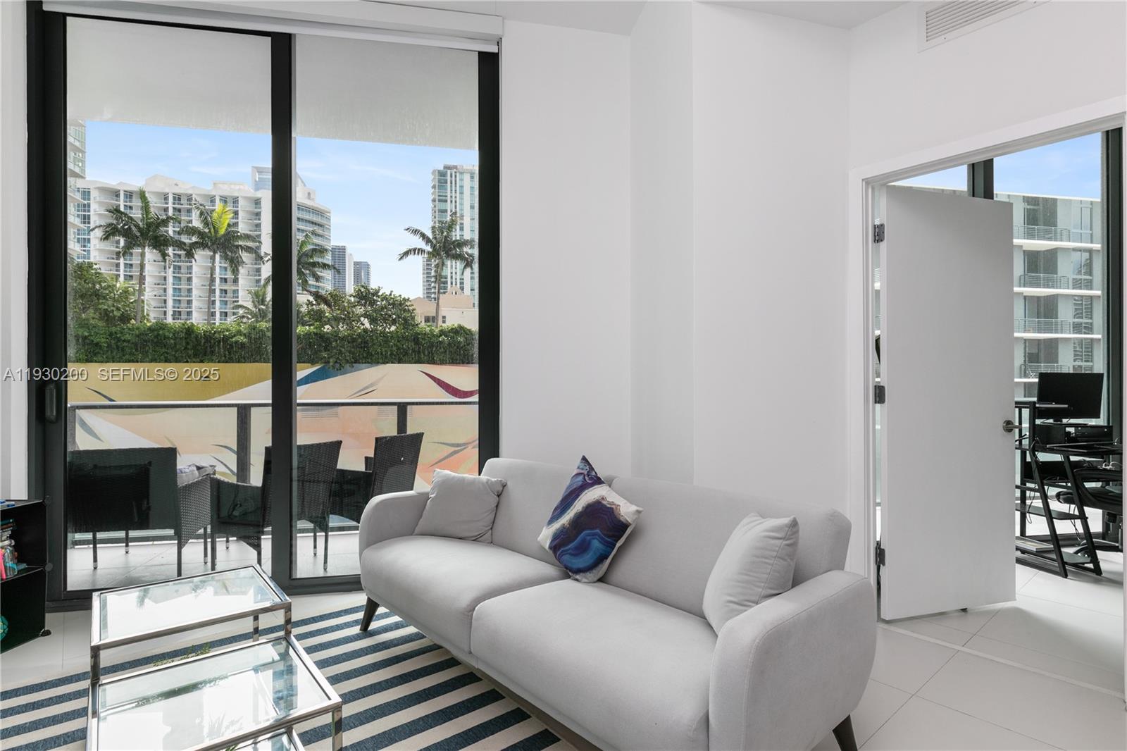 A living room features a light gray sofa, a striped rug, and a balcony view — 501 NE 31st St # 307, Miami FL 33137, MIAMI, FL