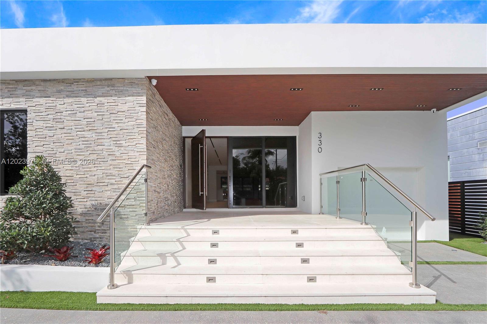 A modern house entrance features stone siding, a wood-paneled ceiling, and glass-railed concrete stairs — 330 SW 19th Rd, Miami FL 33129, MIAMI, FL