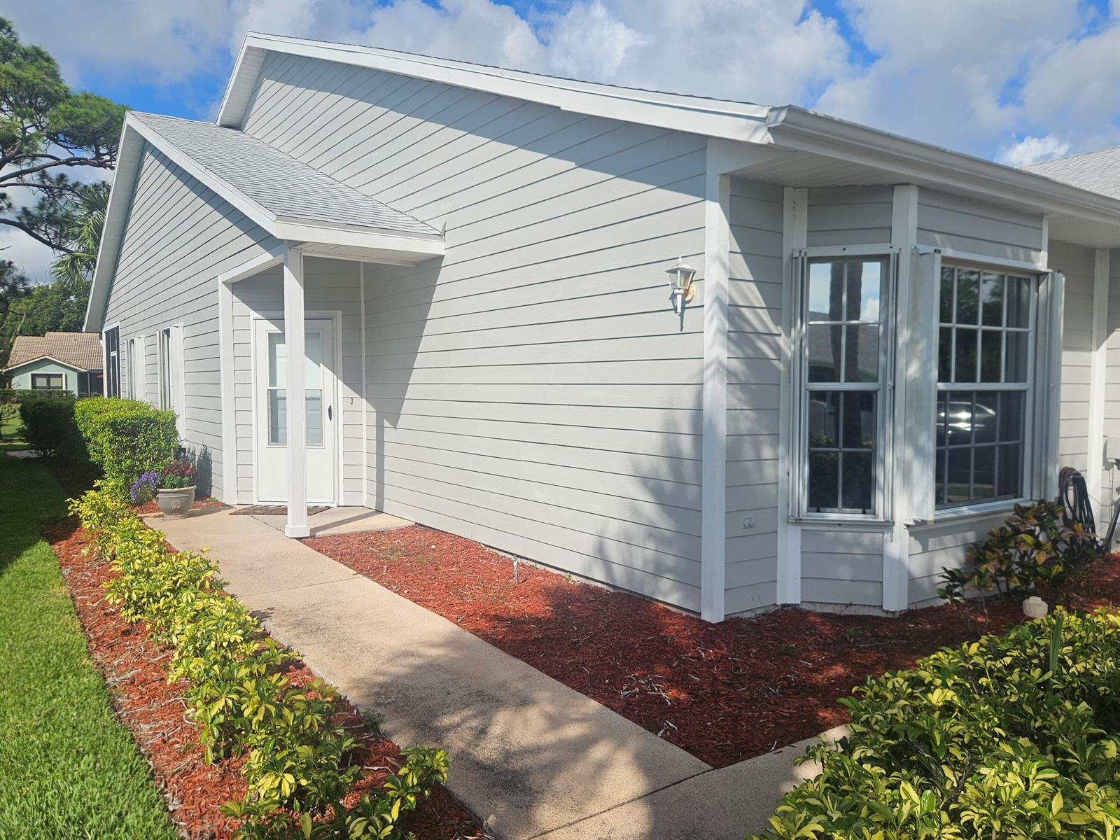 A light gray house exterior features a concrete walkway, a white door, and bay windows — 4011 Gator Trace Road, Fort Pierce FL 34982, FORT PIERCE, FL