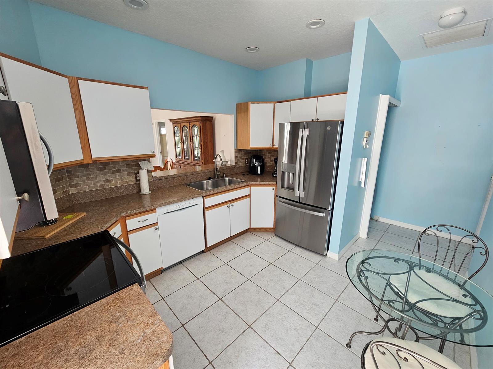 A kitchen features light blue walls, white cabinets, stainless steel appliances, and tile flooring — 4011 Gator Trace Road, Fort Pierce FL 34982, FORT PIERCE, FL