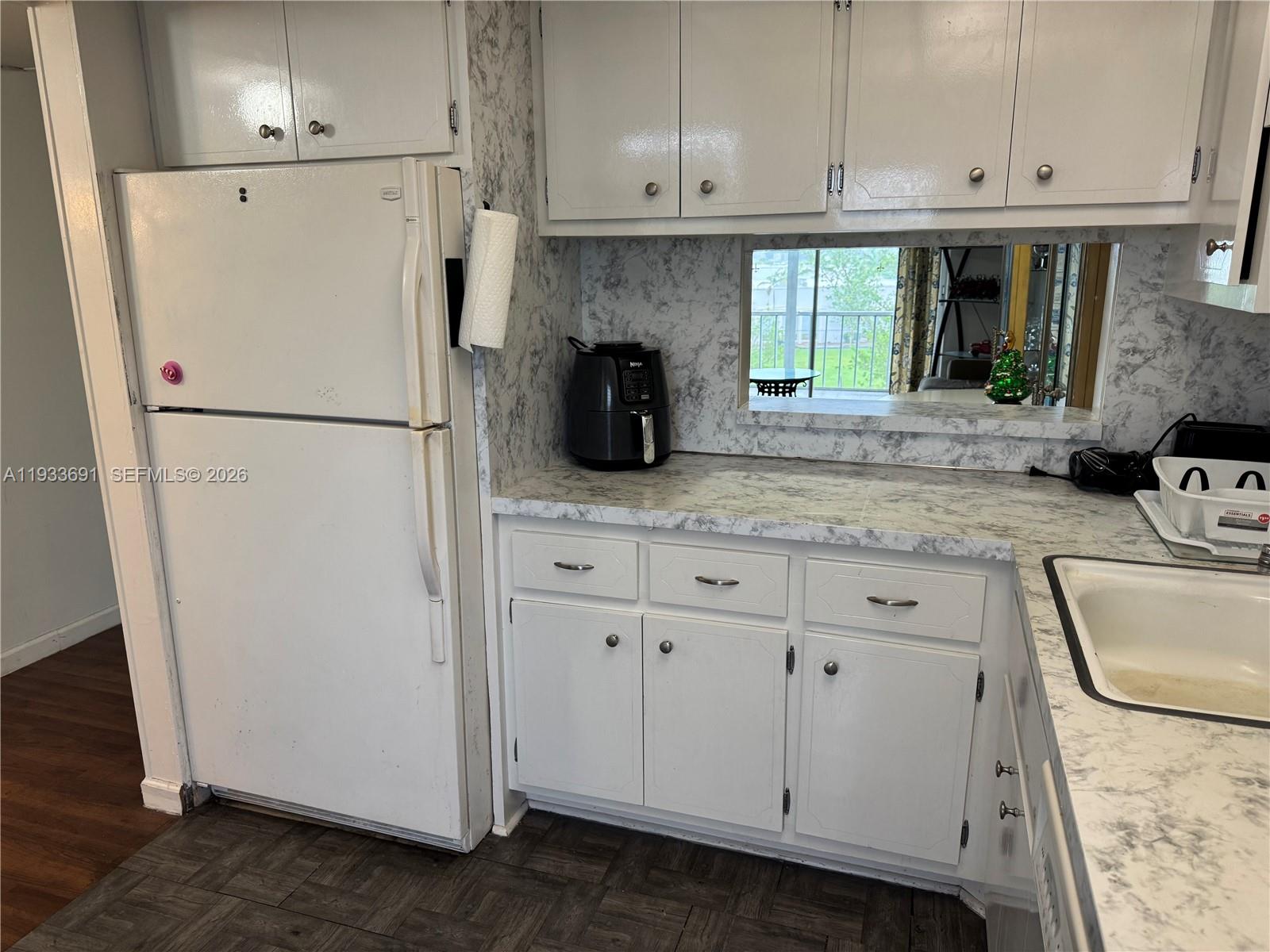 A kitchen features white cabinets, marble-patterned countertops, a white refrigerator, and a pass-through window — 950 Hillcrest Dr # 411, Hollywood FL 33021, HOLLYWOOD, FL