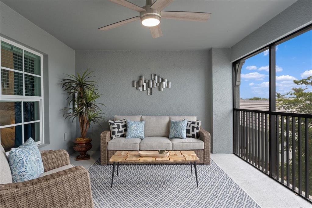 A covered balcony features a wicker sofa, a coffee table, and a ceiling fan — 12440 WELLEN GOLF STREET UNIT 204, VENICE, FL