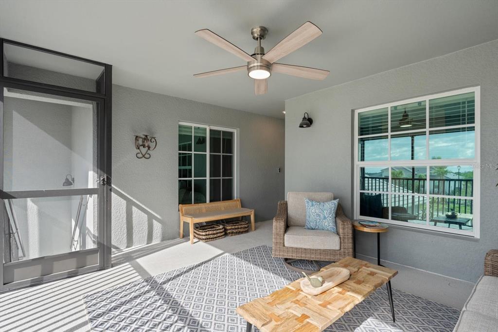 A covered patio features a ceiling fan, wicker armchair, wooden coffee table, and a screen door — 12440 WELLEN GOLF STREET UNIT 204, VENICE, FL