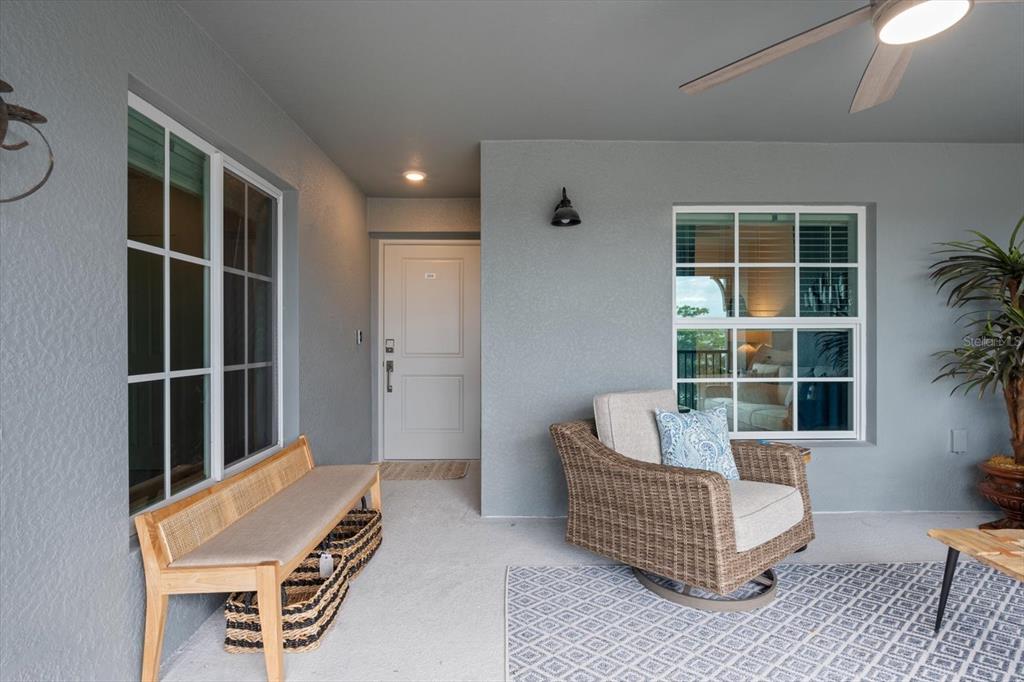 A covered patio features a wicker chair, a wooden bench, and a white entry door — 12440 WELLEN GOLF STREET UNIT 204, VENICE, FL