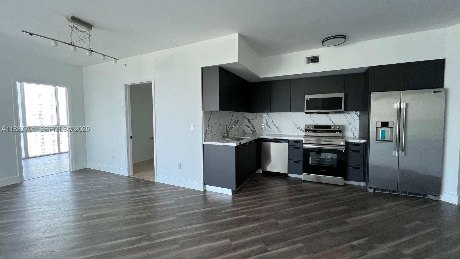 A modern kitchen features dark cabinetry, stainless steel appliances, and marble-patterned backsplash against wood flooring — 350 S Miami Ave # 2401, Miami FL 33130, MIAMI, FL