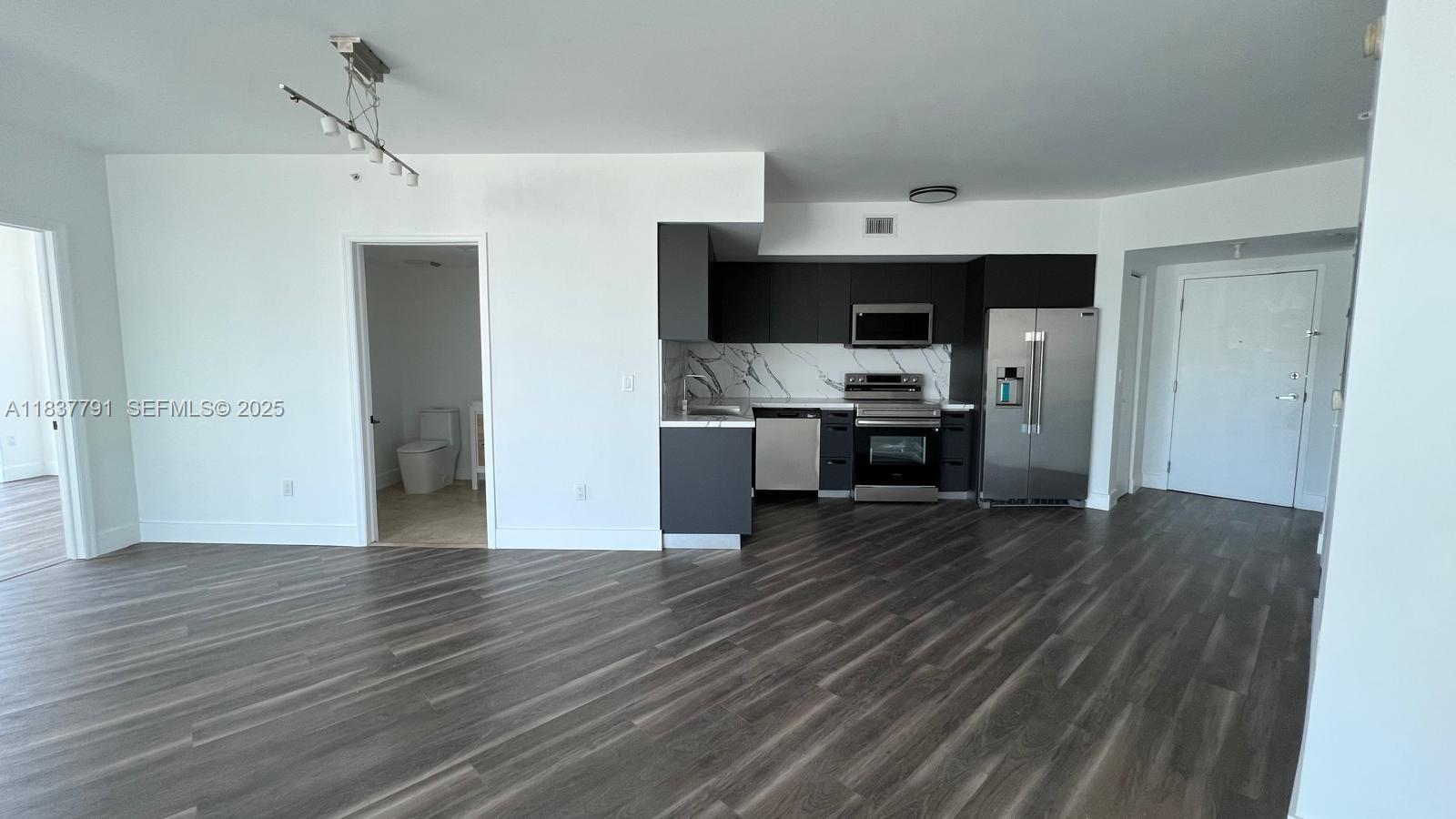 A modern kitchen with dark cabinetry and stainless steel appliances opens into a living area — 350 S Miami Ave # 2401, Miami FL 33130, MIAMI, FL