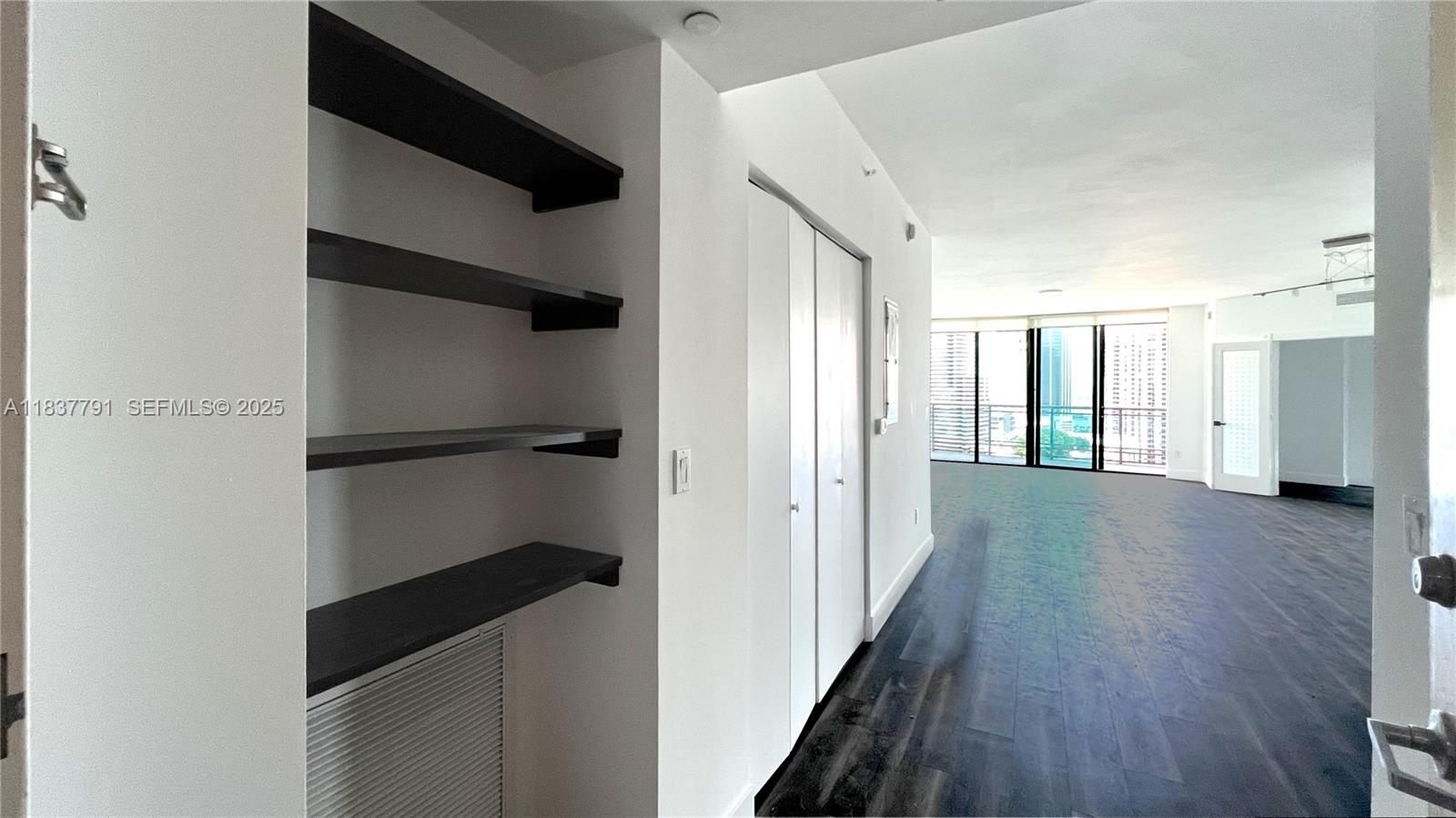 An interior view shows a hallway with dark wood floors, built-in shelves, and a living area — 350 S Miami Ave # 2401, Miami FL 33130, MIAMI, FL
