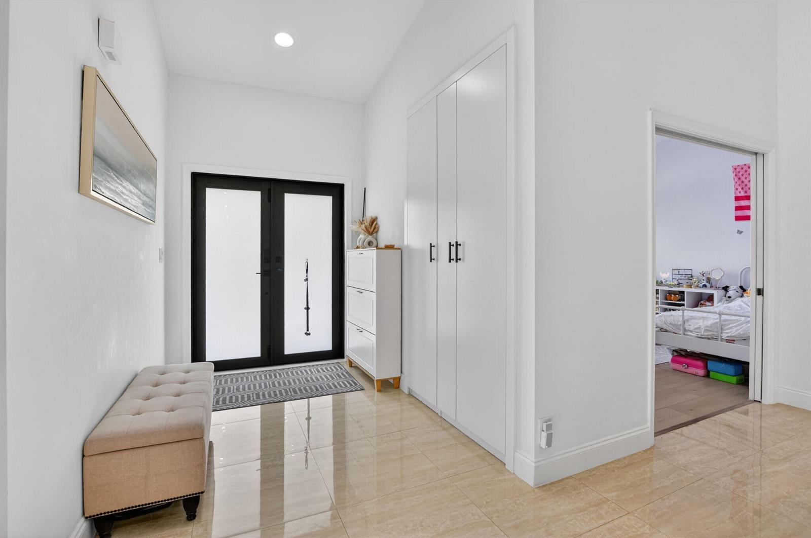 A bright entryway features a tufted bench, white storage cabinets, and a black-framed double door — 19700 Sedgefield Terrace, Boca Raton FL 33498, BOCA RATON, FL