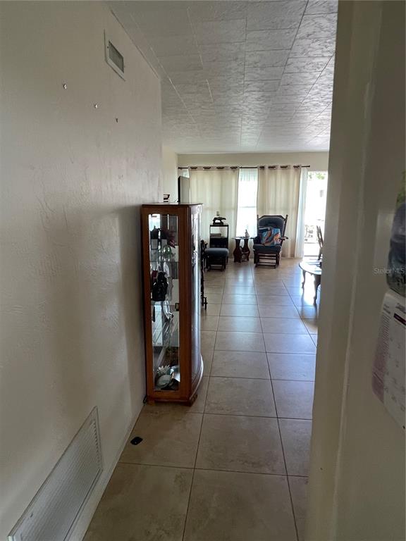 A hallway with tile flooring leads toward a living area with large windows and curtains — 4144 57TH STREET N UNIT 269, KENNETH CITY, FL