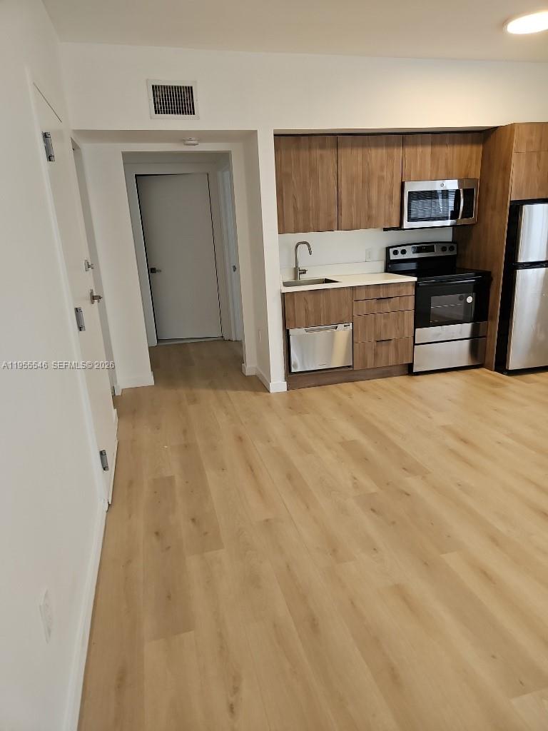 A kitchen with wood-tone cabinets and stainless steel appliances opens to a living area — 557 Michigan Ave, Miami Beach FL 33139, MIAMI BEACH, FL