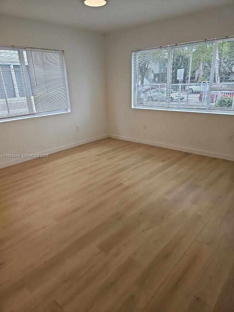 An empty room features light wood-look flooring, white walls, and windows with horizontal blinds — 557 Michigan Ave, Miami Beach FL 33139, MIAMI BEACH, FL