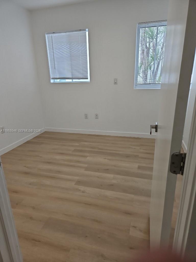 An empty bedroom features white walls, light wood-look flooring, and two windows with blinds — 557 Michigan Ave, Miami Beach FL 33139, MIAMI BEACH, FL