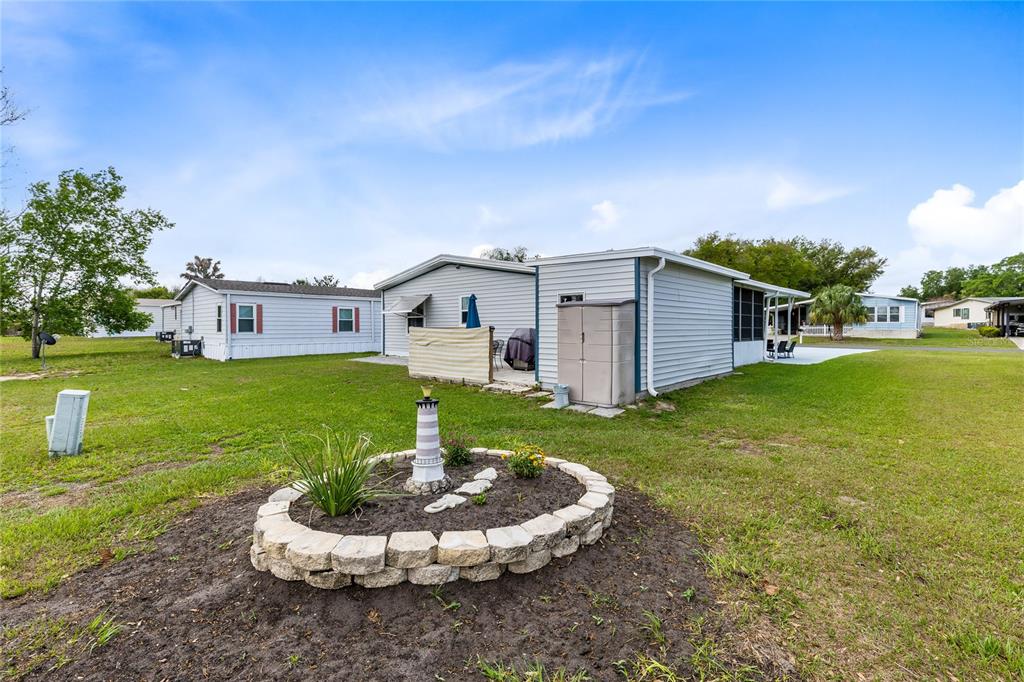 A backyard view of a manufactured home with a stone-bordered garden bed and lighthouse ornament — 516 RANGER PARK COURT, DAVENPORT, FL