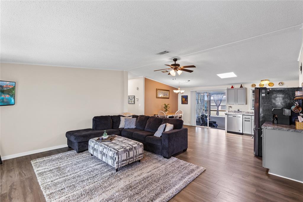 An open-concept living room features a dark sectional sofa, a patterned ottoman, and wood flooring — 516 RANGER PARK COURT, DAVENPORT, FL