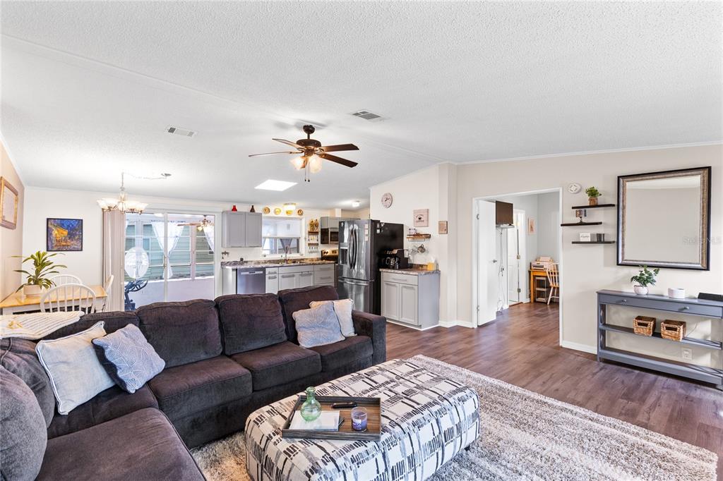 A living room with a dark sectional sofa, patterned ottoman, and an open-concept kitchen — 516 RANGER PARK COURT, DAVENPORT, FL