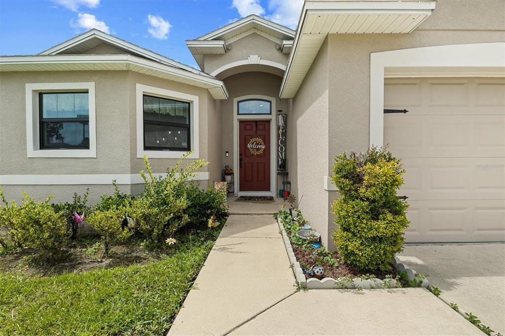 A beige house exterior features a red front door, a concrete walkway, and landscaping — 133 CROSSING DRIVE, LAKELAND, FL