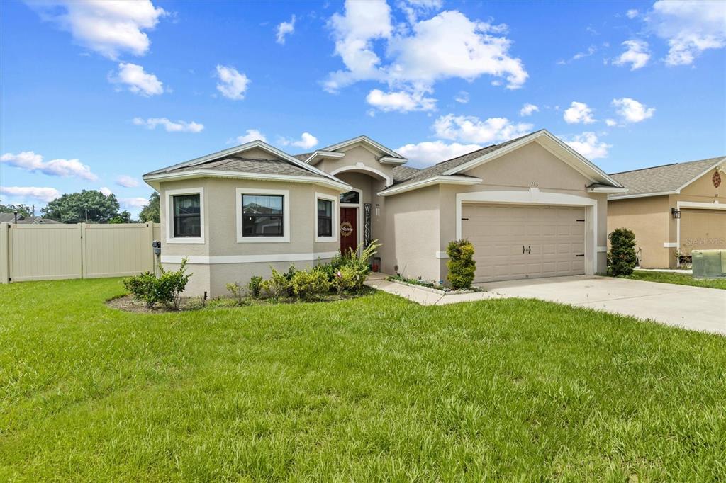 A single-story suburban house with a beige stucco exterior, a two-car garage, and front landscaping — 133 CROSSING DRIVE, LAKELAND, FL