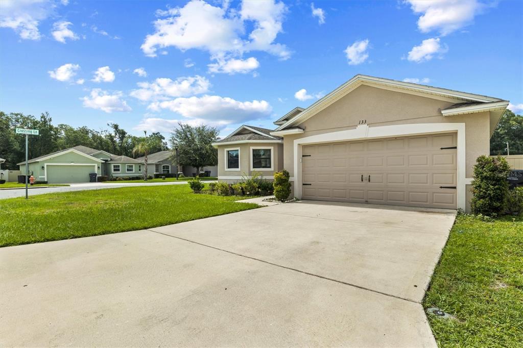 A beige single-story house with a two-car garage and a concrete driveway — 133 CROSSING DRIVE, LAKELAND, FL