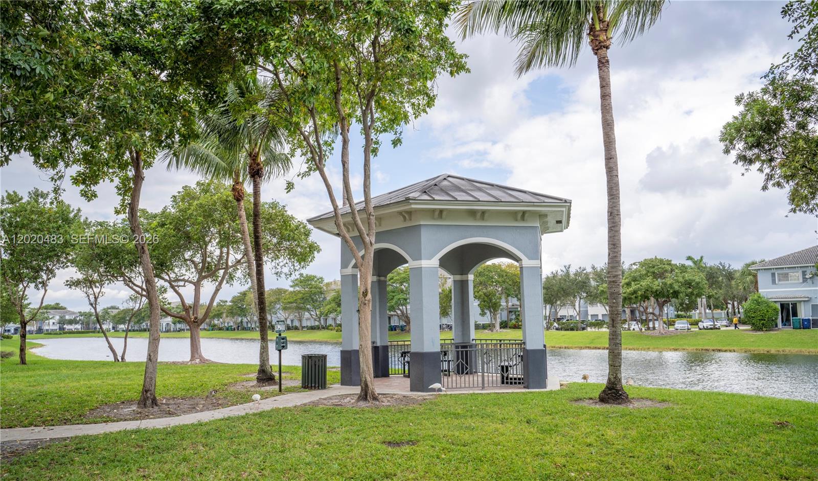 A gray gazebo sits on a grassy lawn beside a lake with palm trees — 1415 NW 34th Way, Lauderhill FL 33311, LAUDERHILL, FL
